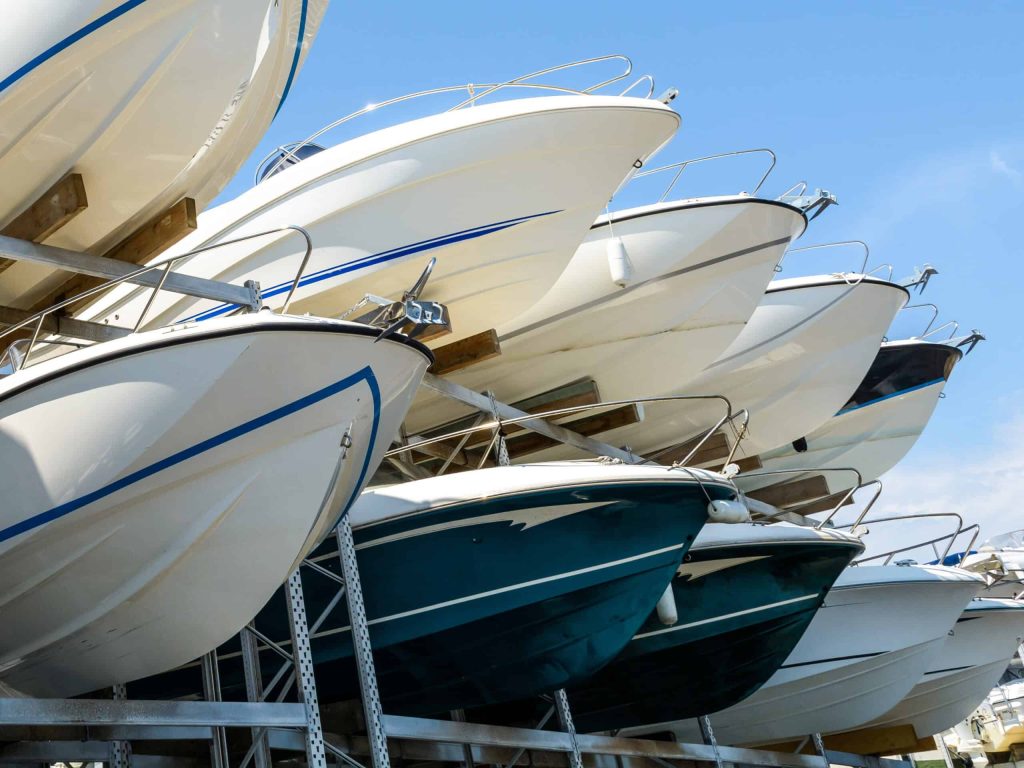 View from below of the hulls of motorboats racked one above another on two levels in a dry rack boat storage facility against blue sky.