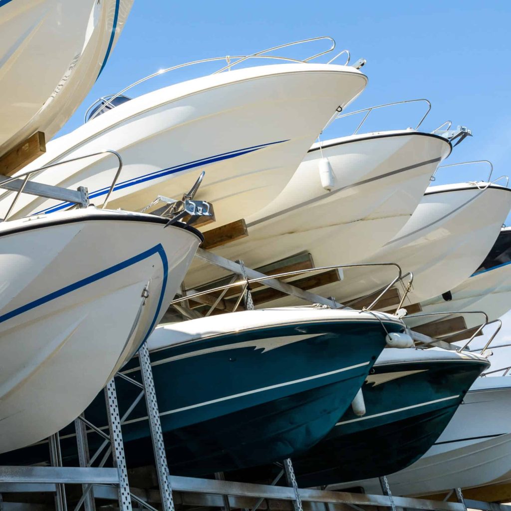 View from below of the hulls of motorboats racked one above another on two levels in a dry rack boat storage facility against blue sky.